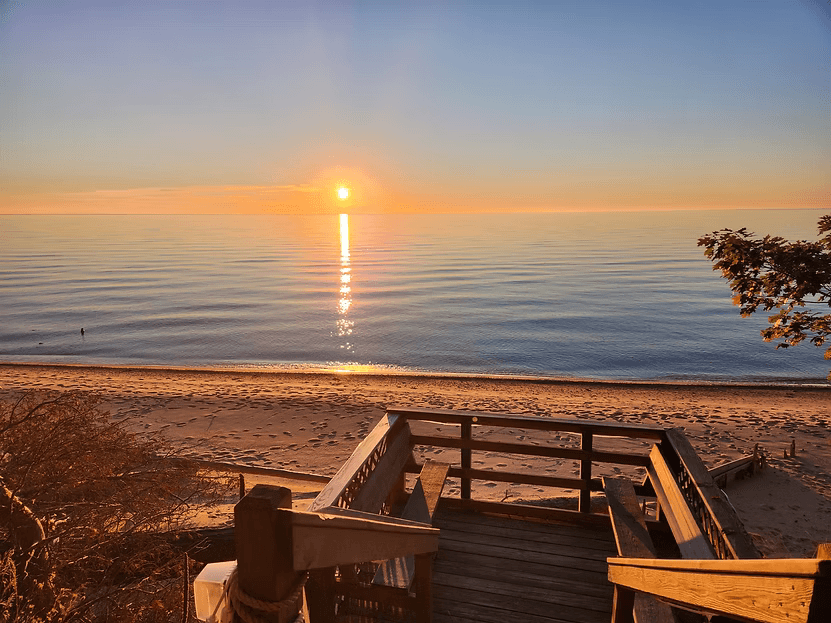 A serene beach scene at sunset with a wooden staircase leading down to the shore.