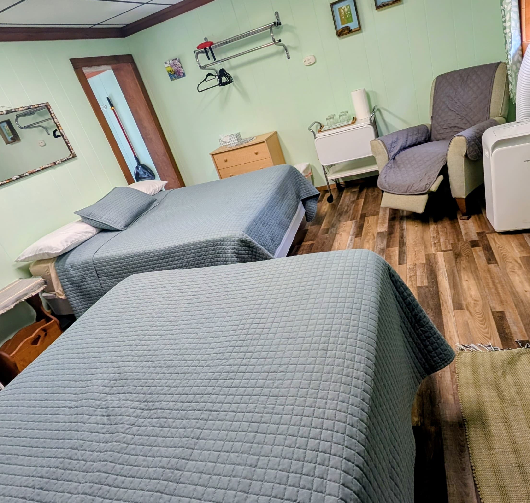 A cozy bedroom featuring two twin beds, a chair, and light green walls.
