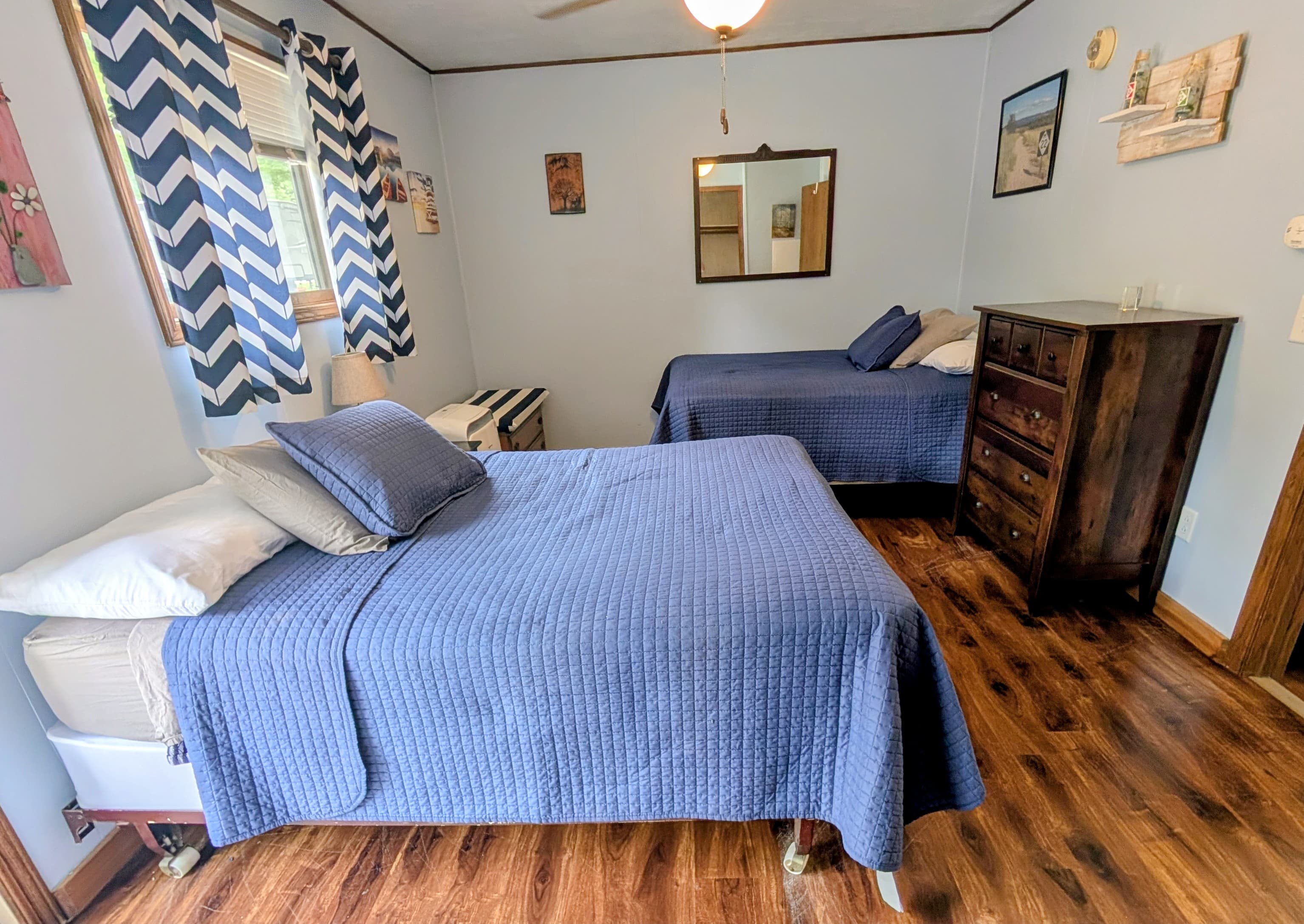 A cozy bedroom featuring two neatly made beds with blue bedding and wooden furniture.