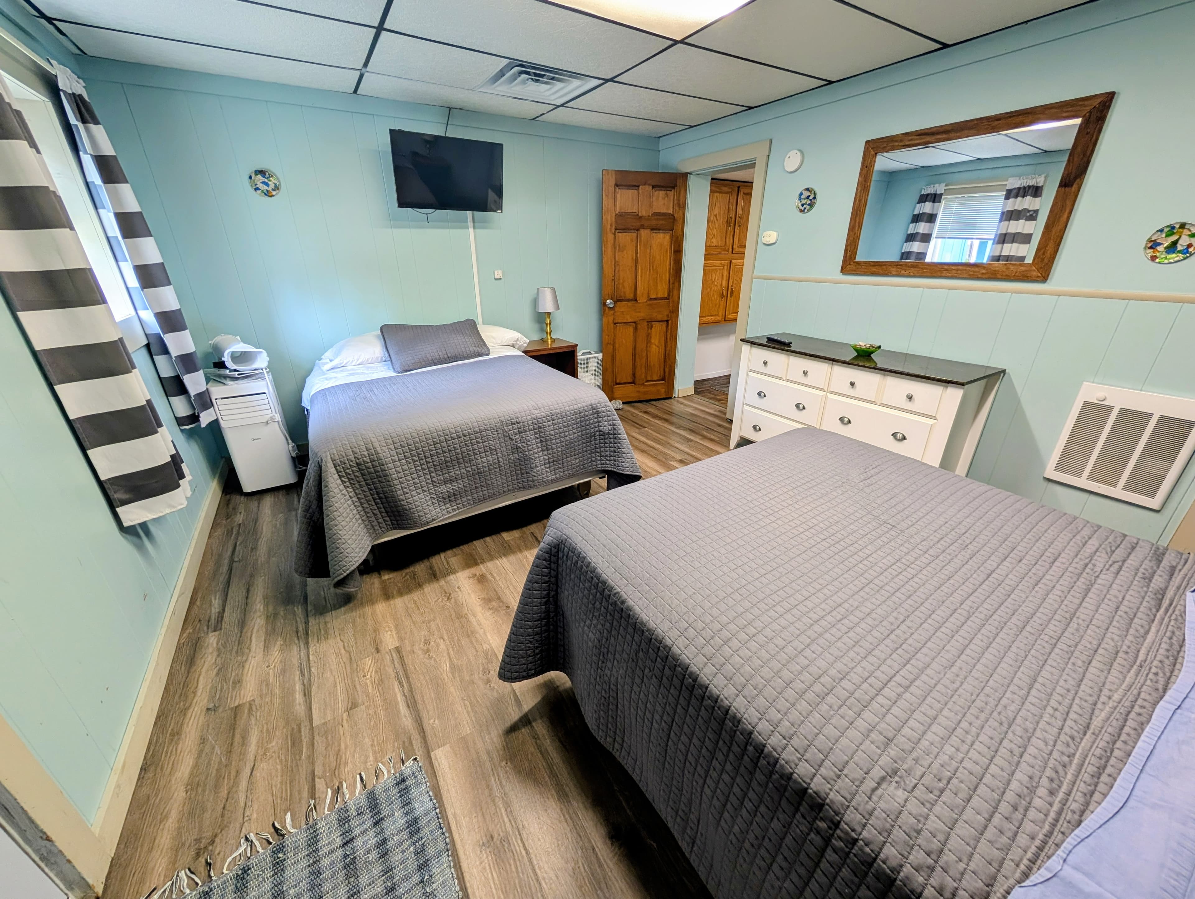 A tidy guest room featuring two beds, a TV, and a small dresser against a mint-green wall.