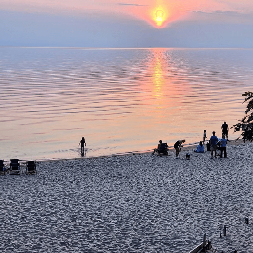 A serene beach scene at sunset with people enjoying the water and sand.