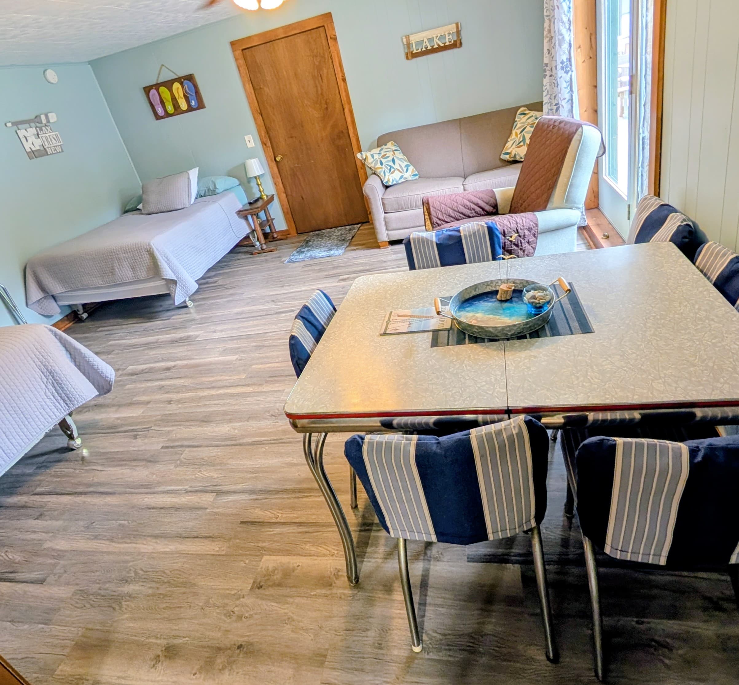 A cozy living space featuring a dining table, a sofa, and two beds with natural light coming through the windows.