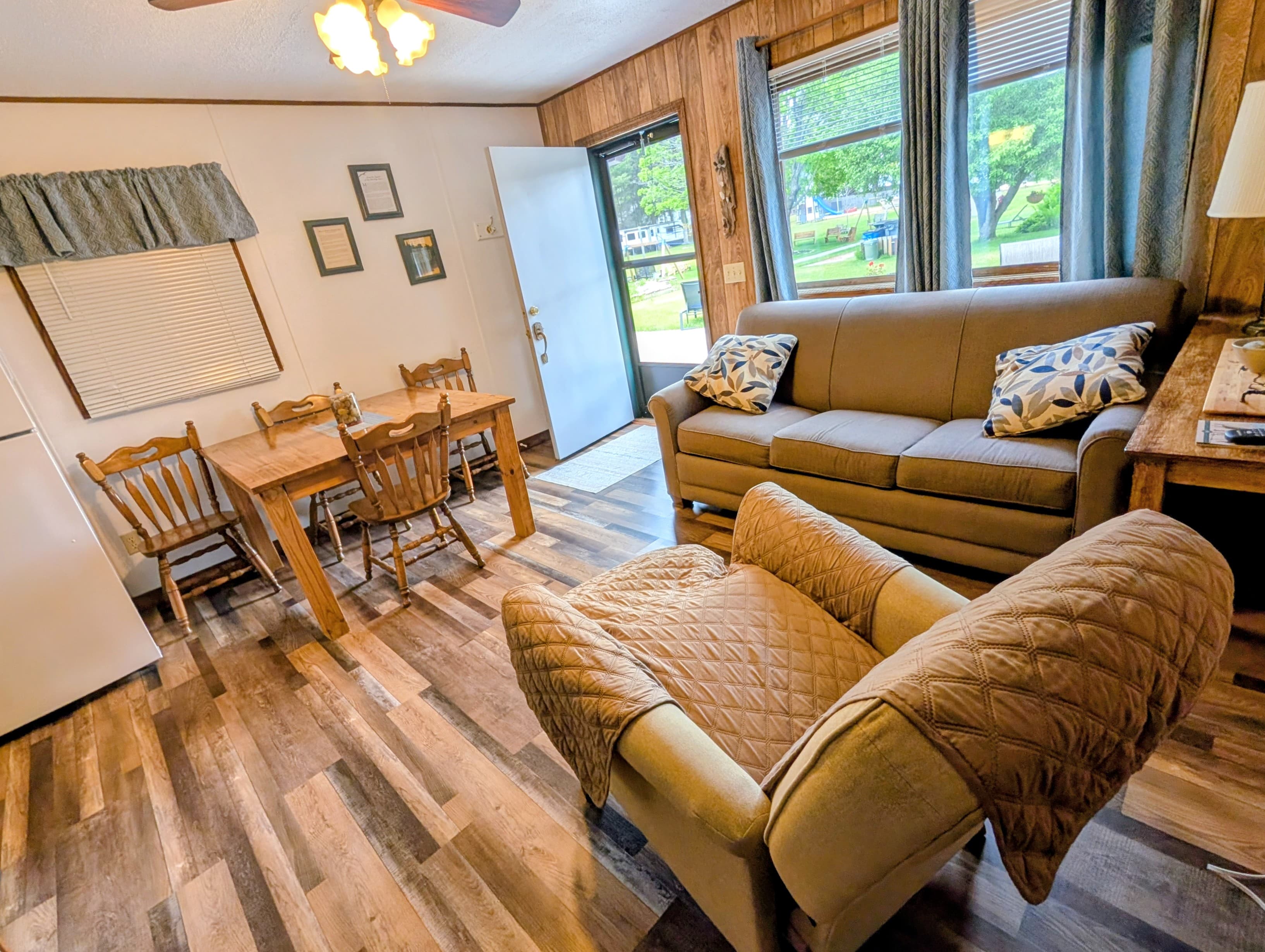 Cozy living space featuring a sofa, armchair, dining table, and large windows.