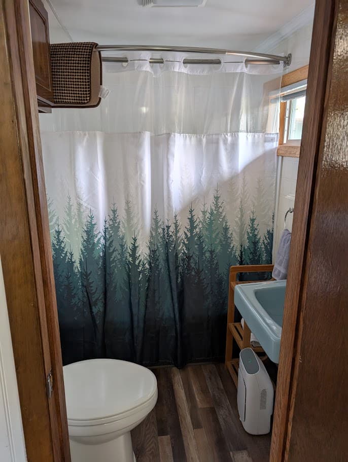 A bathroom featuring a forest-themed shower curtain, a toilet, and wooden accents.