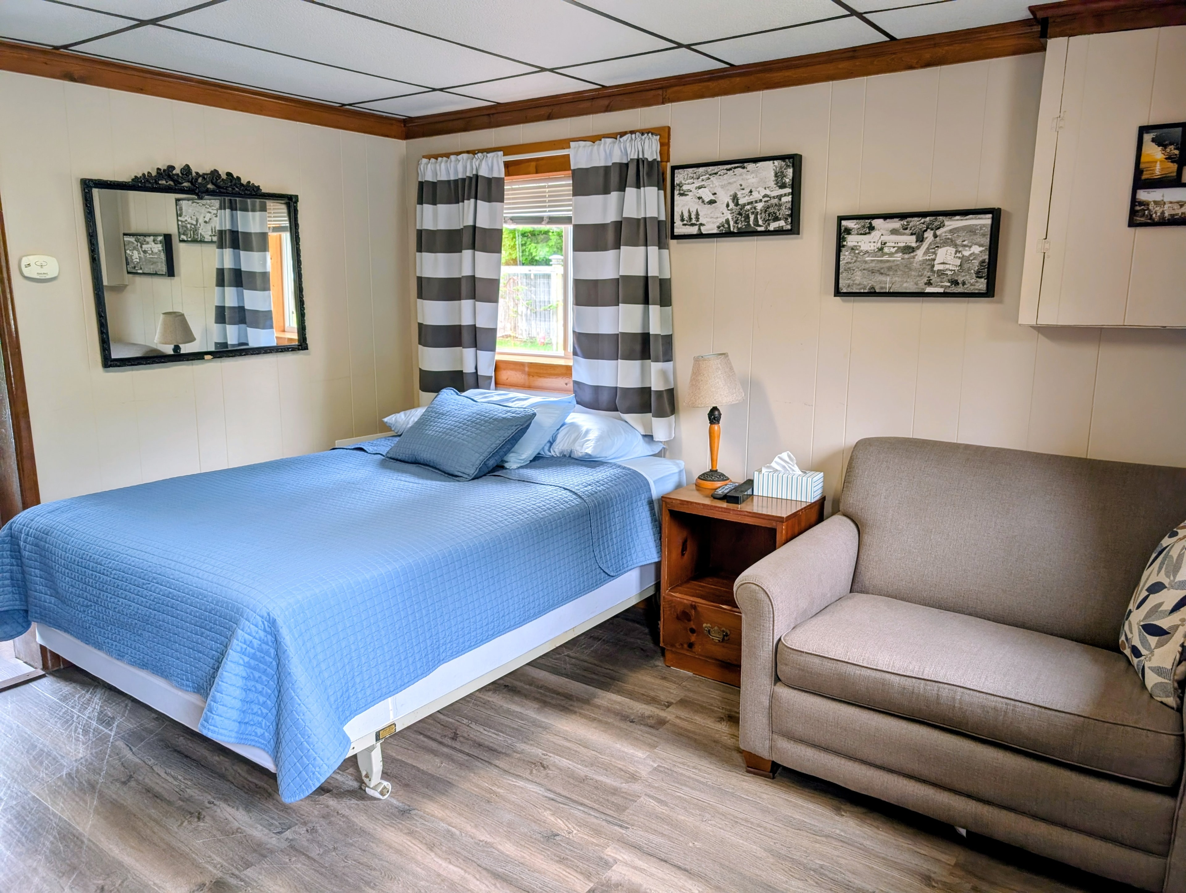 A cozy bedroom featuring a queen bed, a light gray sofa, and framed photographs on the walls.
