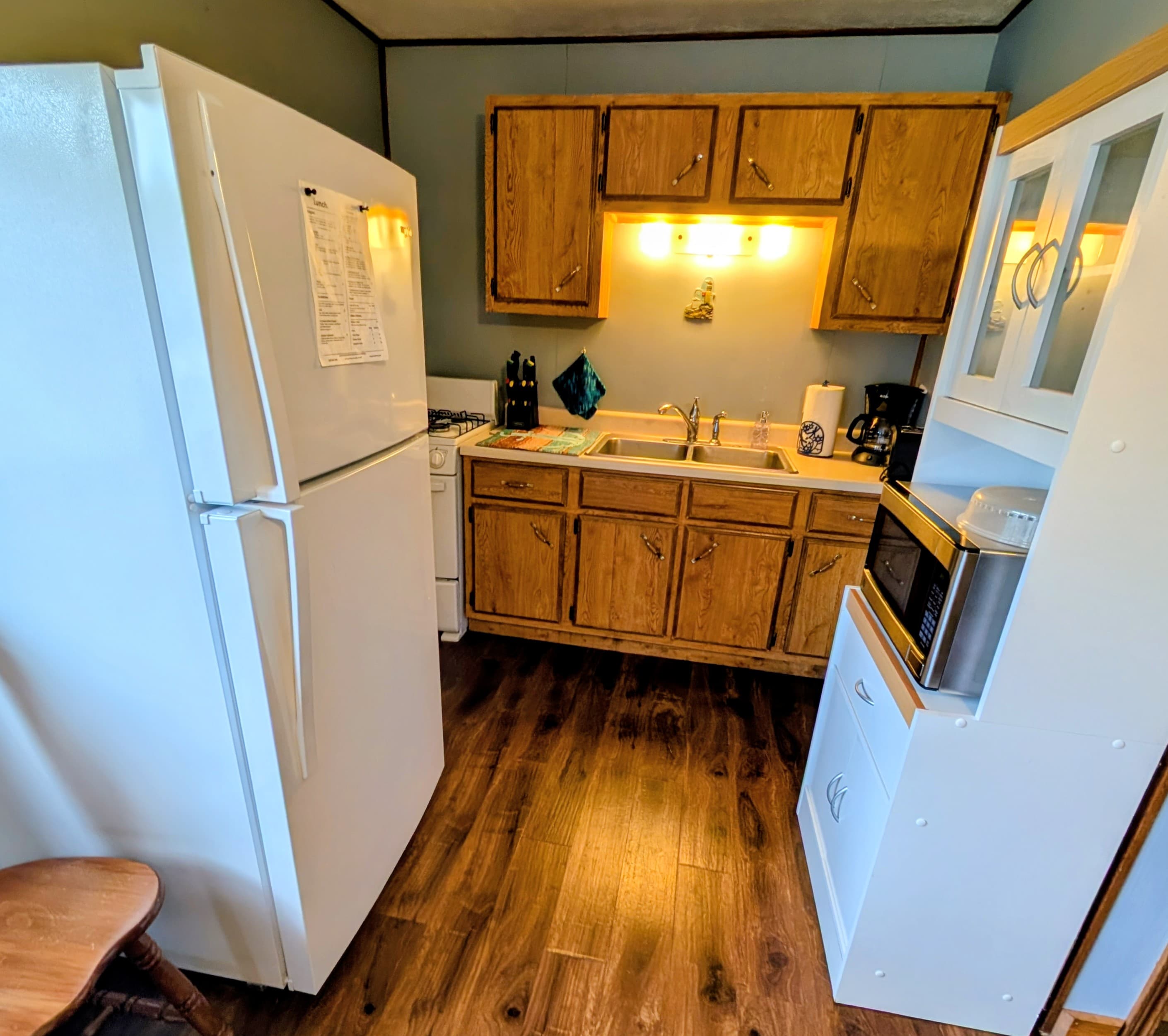 A compact kitchen featuring wooden cabinets, a refrigerator, stove, and microwave.