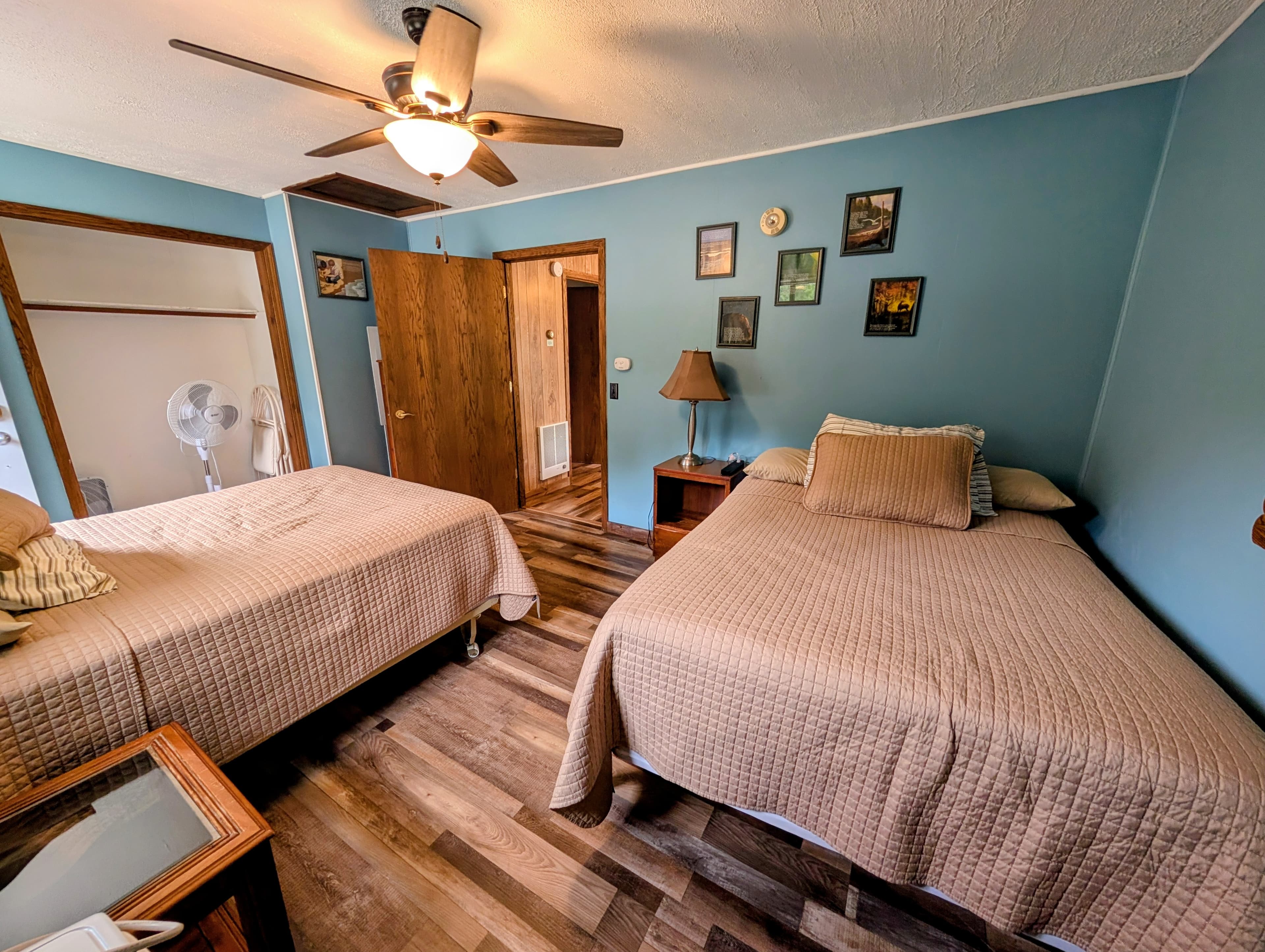 A cozy bedroom featuring two twin beds, wooden flooring, and a ceiling fan.