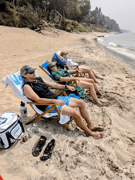 Four people relax on beach chairs along a sandy shoreline.