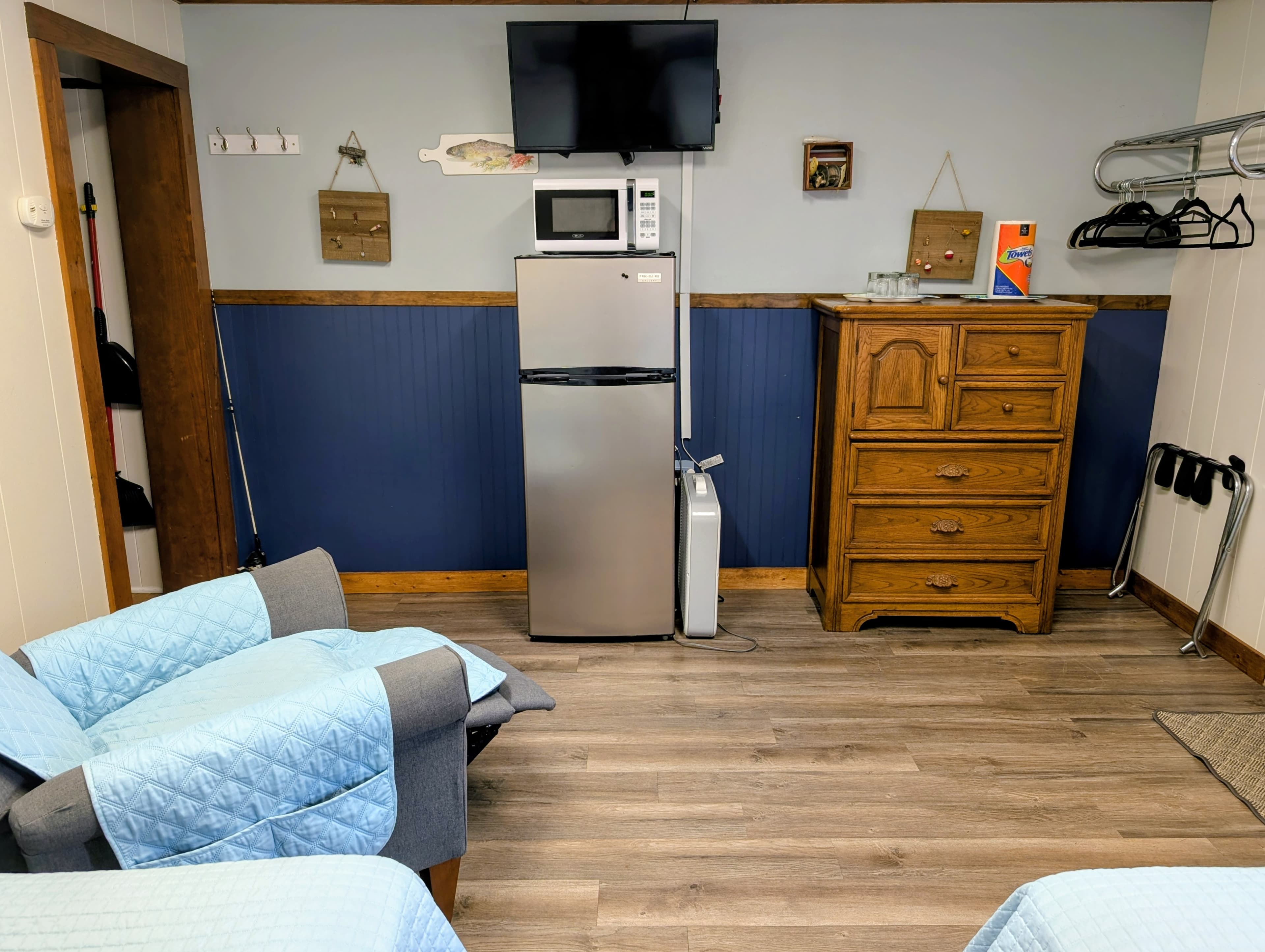 A cozy room featuring two armchairs, a mini-fridge, a microwave, a TV, and a wooden dresser against a blue and white wall.