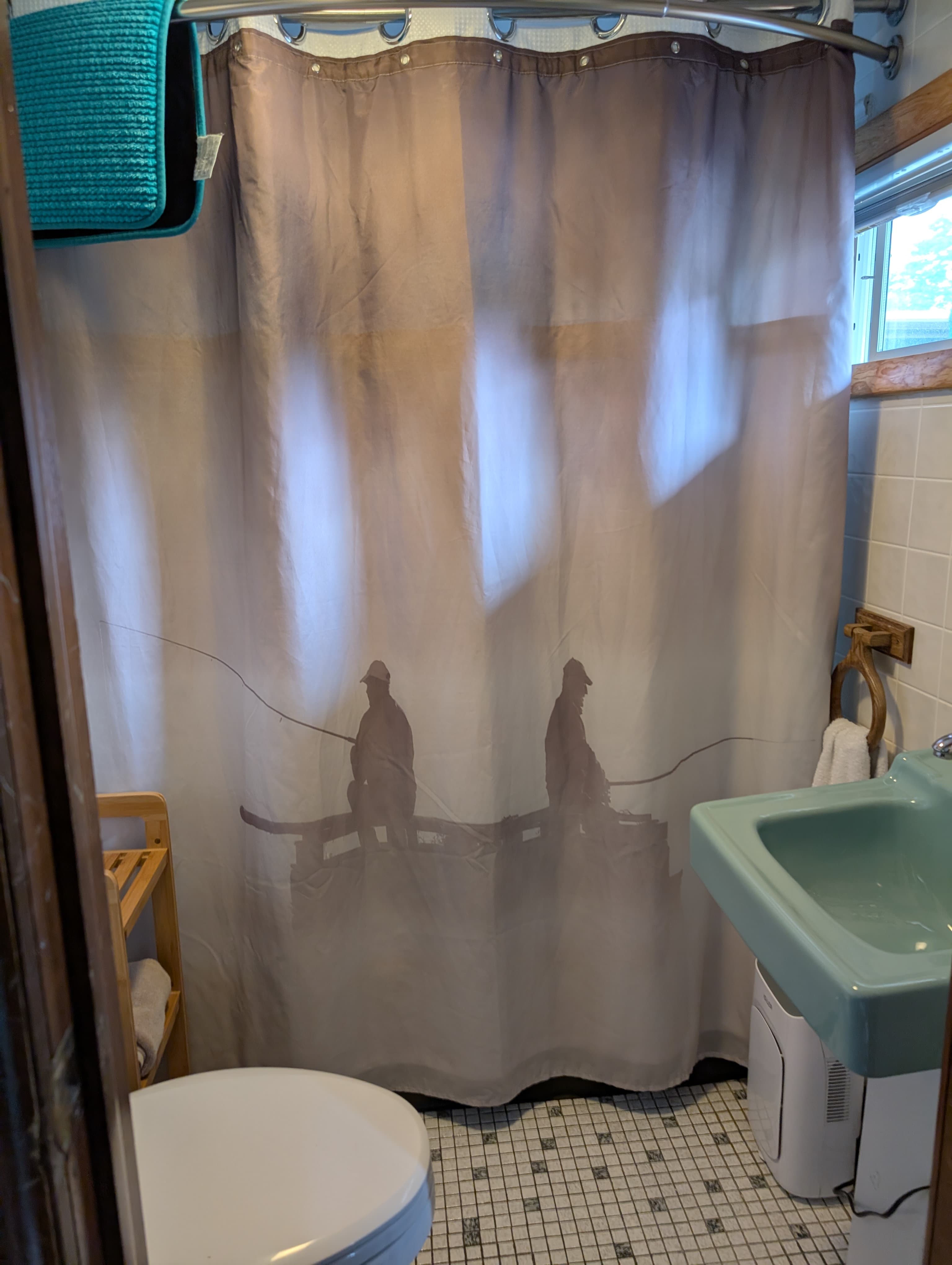 A bathroom featuring a shower curtain with a muted fishing scene silhouette.