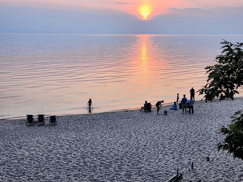 A tranquil beach scene at sunset with people enjoying the water and sand.