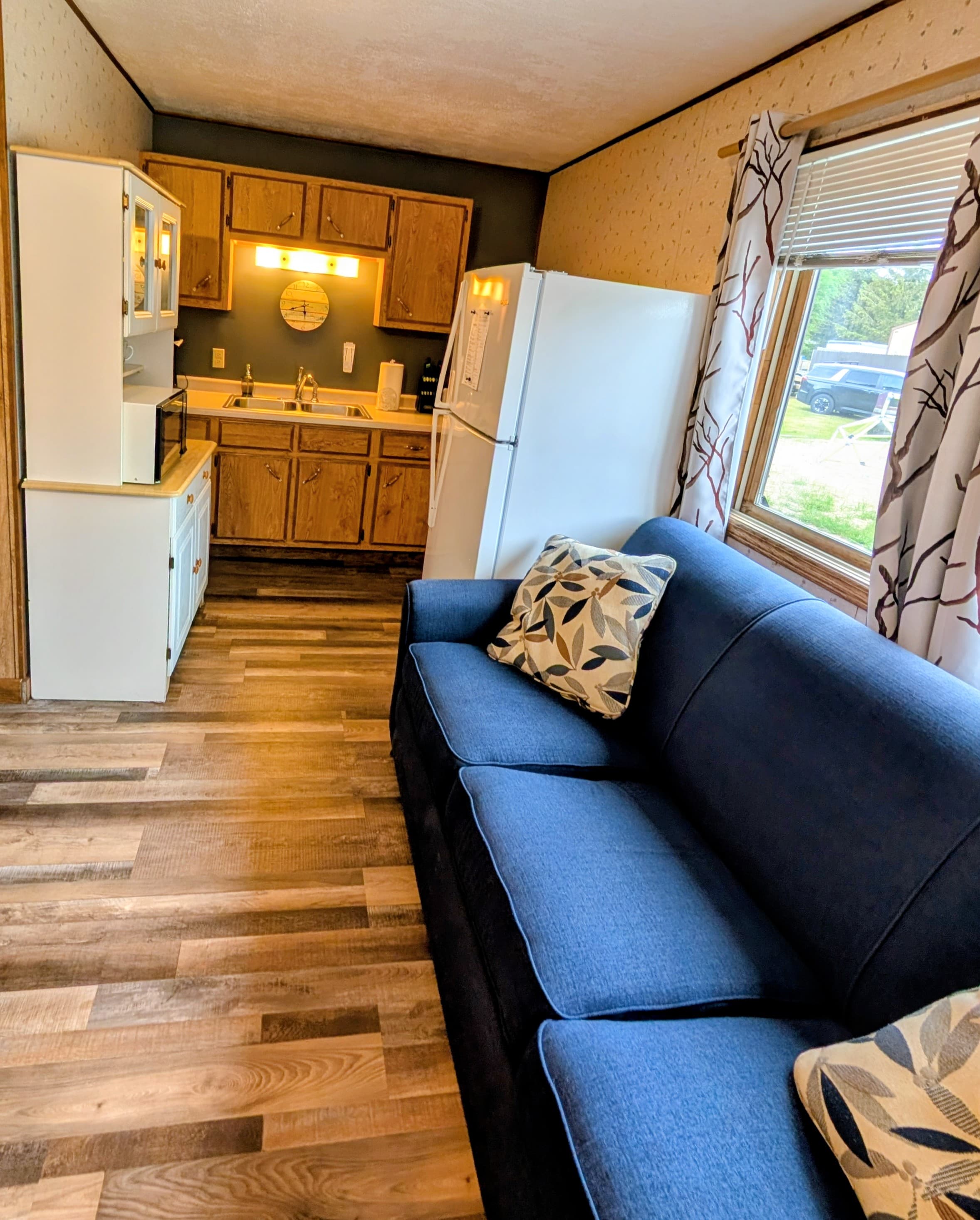 A cozy kitchen and living area with wooden cabinets, a white refrigerator, and a blue couch adorned with decorative pillows.