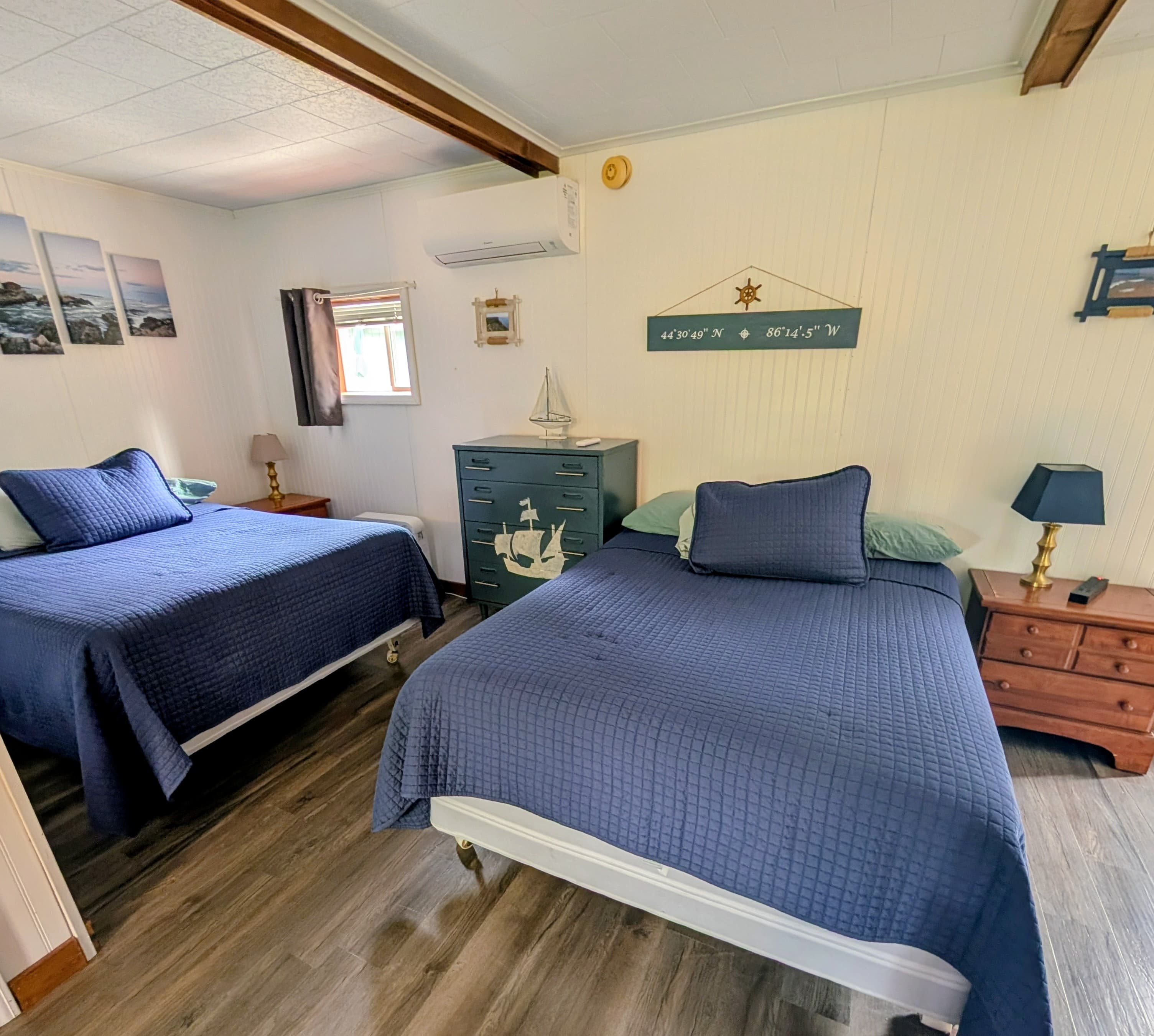A cozy bedroom featuring two beds with navy blue quilts, accented by nautical decor and wooden furniture.