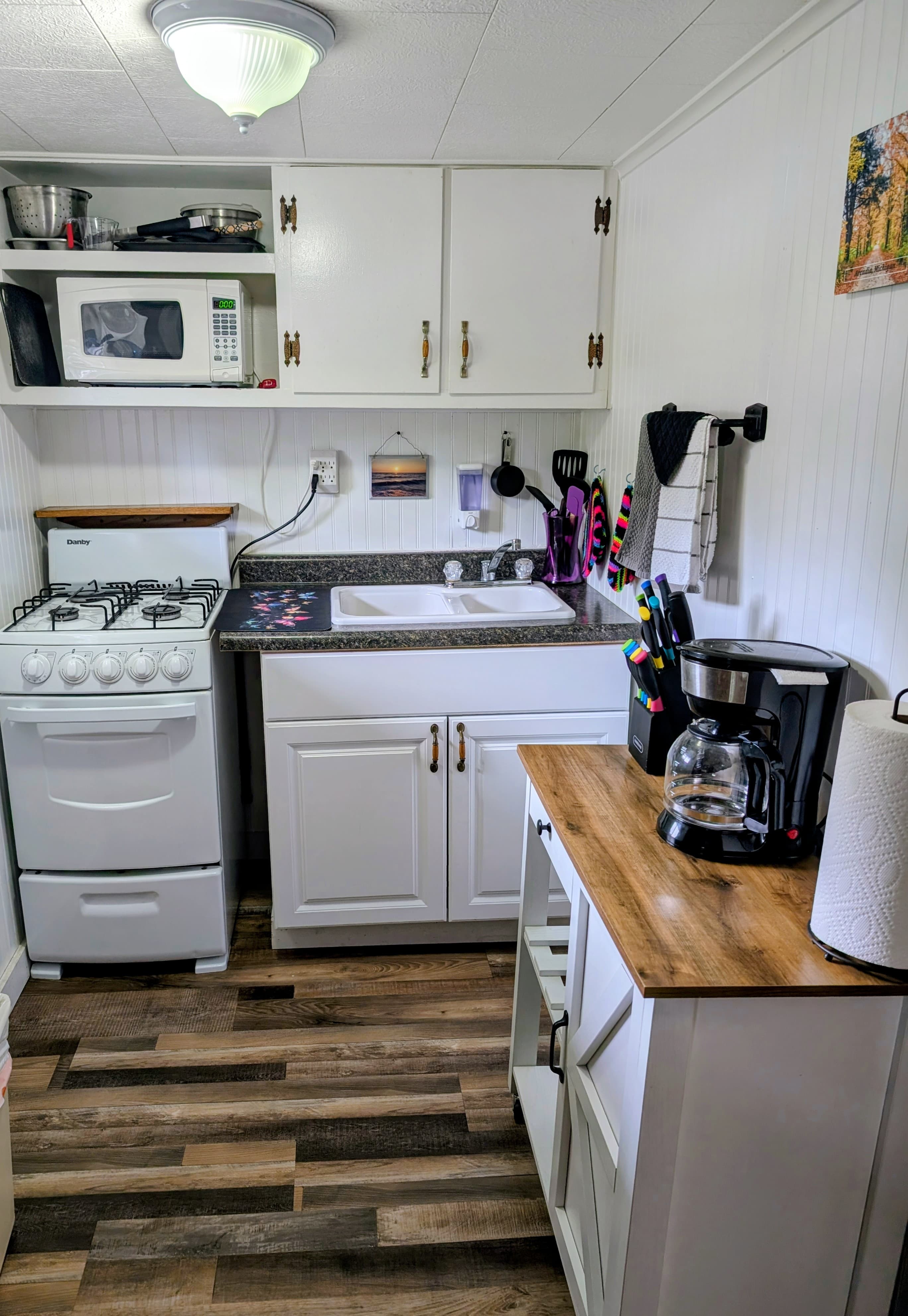 A compact kitchen featuring a gas stove, microwave, sink, and coffee maker with wooden accents.