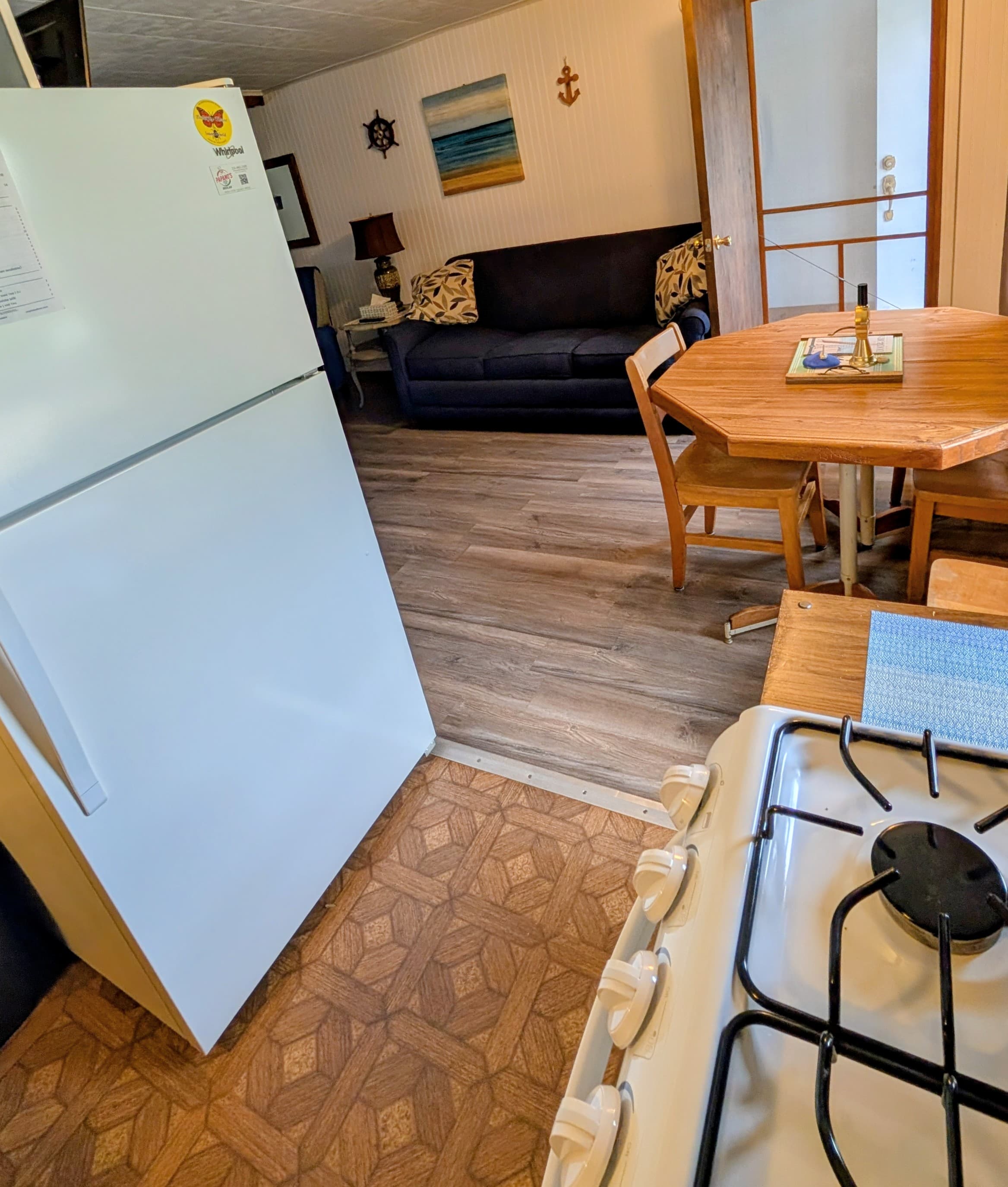 A well-lit kitchen area featuring a refrigerator, stove, and a dining table with chairs, connected to a cozy living space.
