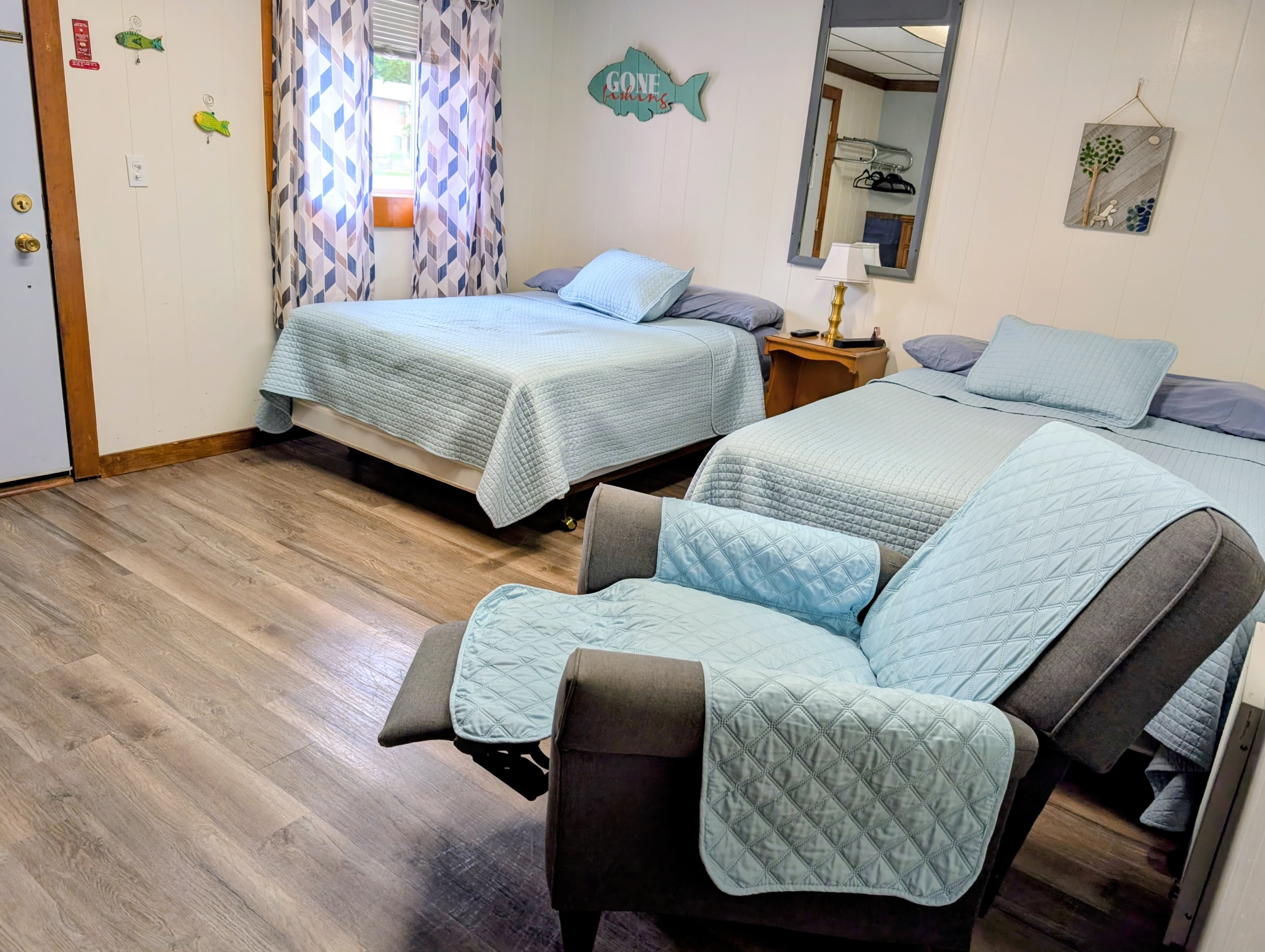 A cozy guest room featuring two beds and a recliner chair with light blue bedding.