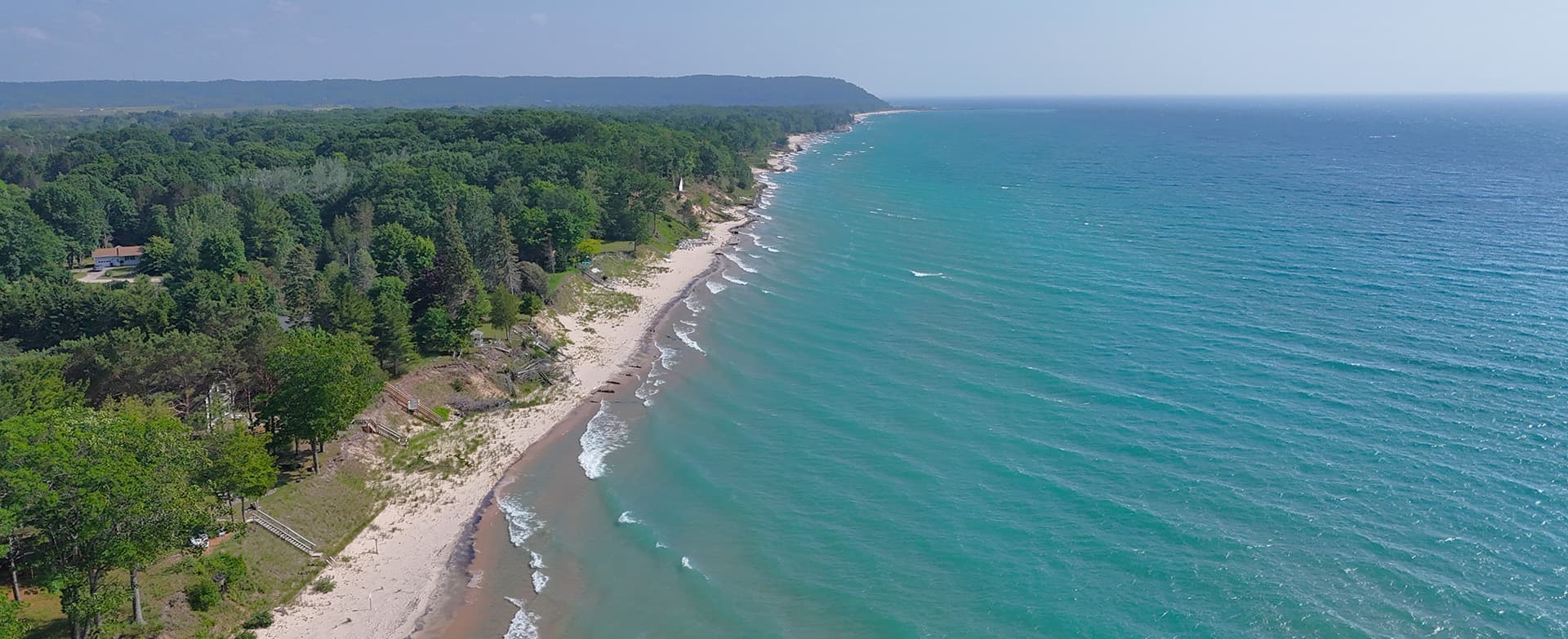 Aerial view of a sandy beach lined with green trees and gentle ocean waves.