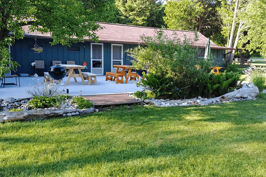 A cozy outdoor patio with picnic tables and lush greenery in front of a blue-green building.