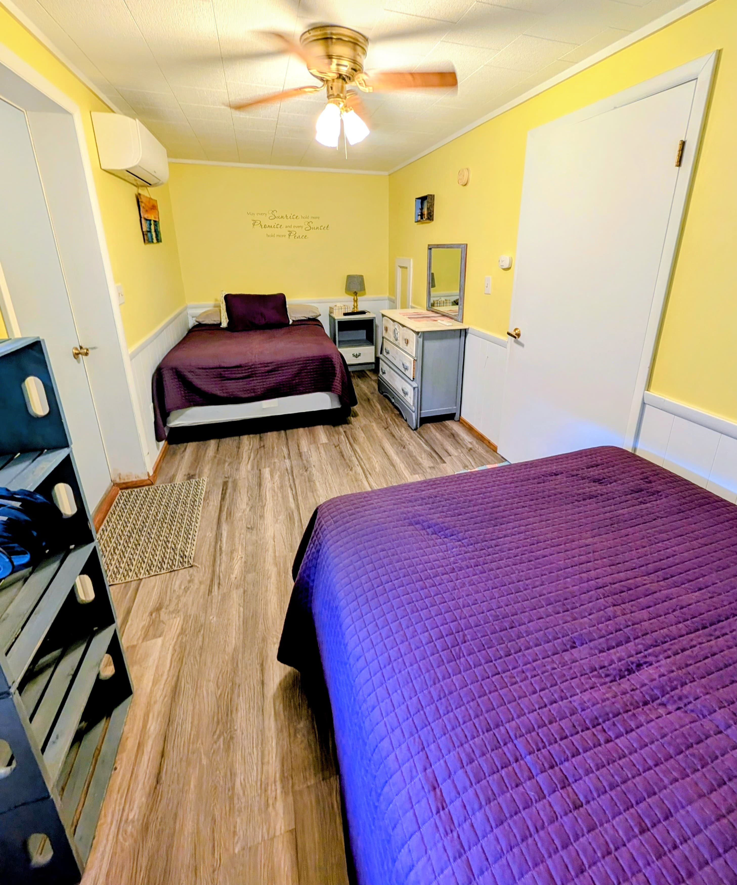 A cozy, yellow-walled bedroom featuring two beds with purple bedding and a dresser.