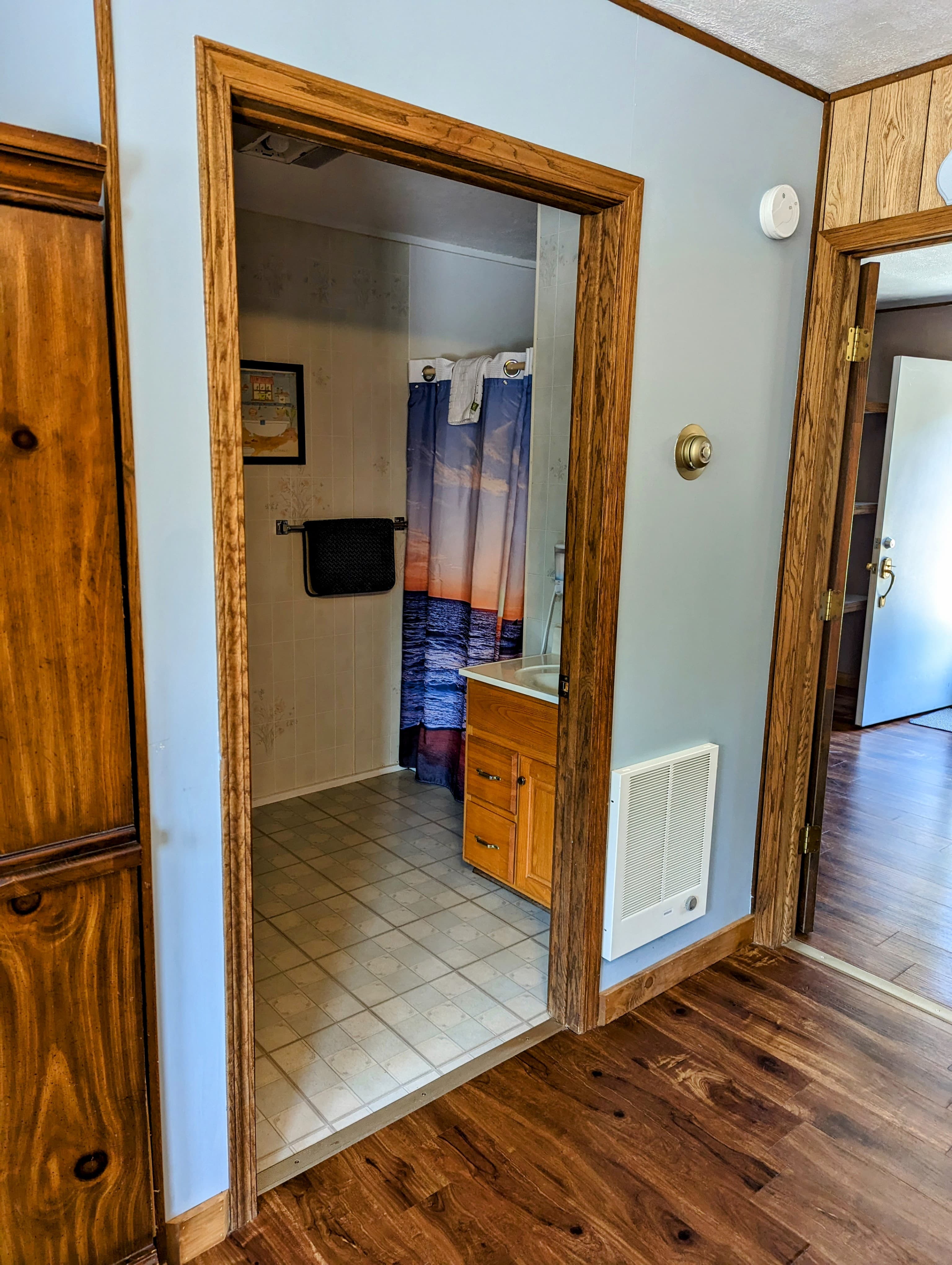 A doorway leading to a small bathroom with a beach-themed shower curtain and a wooden cabinet.