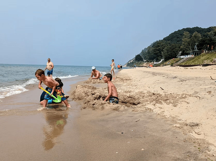 Children playing in the sand at a beach with a few adults in the background.