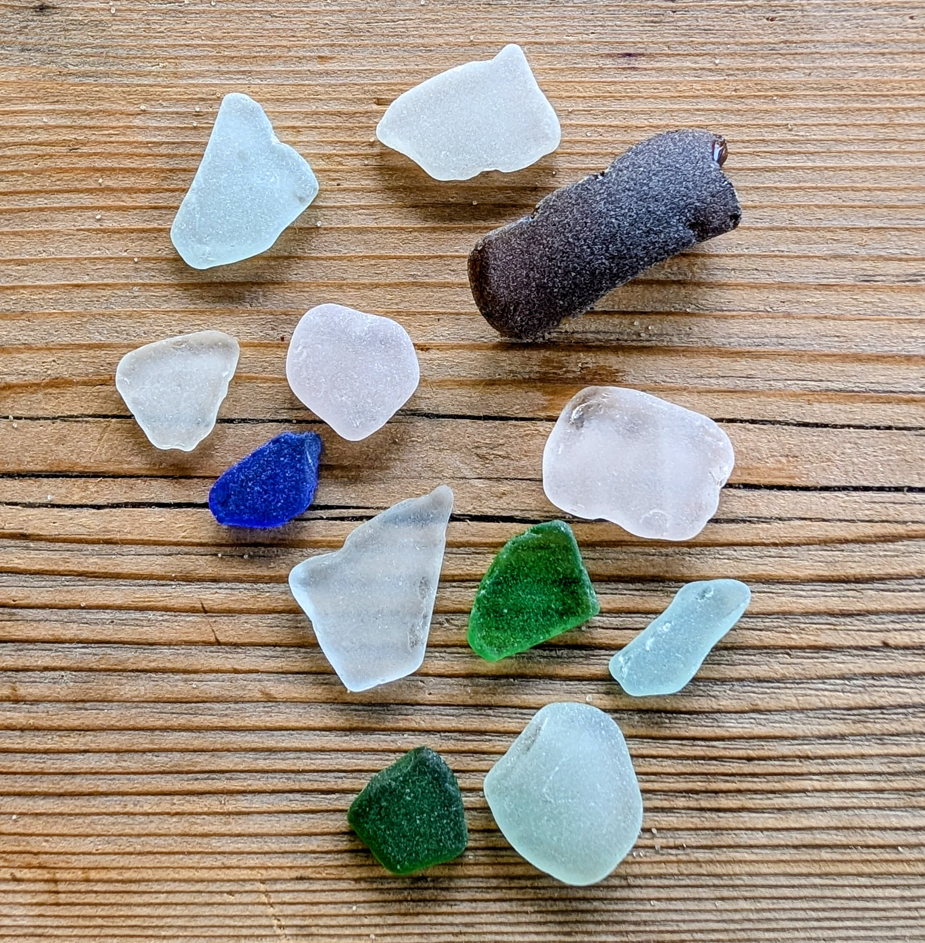 A collection of colorful pieces of sea glass and a small piece of driftwood on a wooden surface.