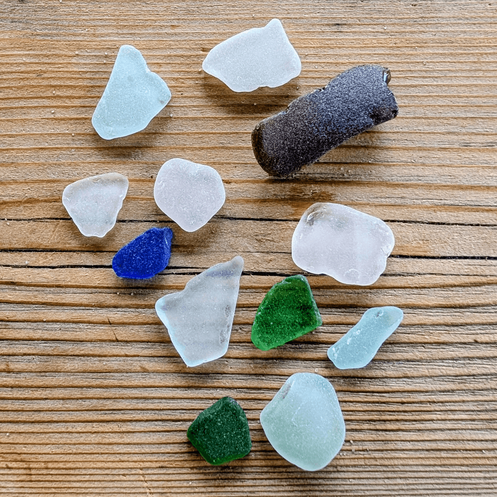 A collection of various pieces of sea glass and a small dark stone on a wooden surface.