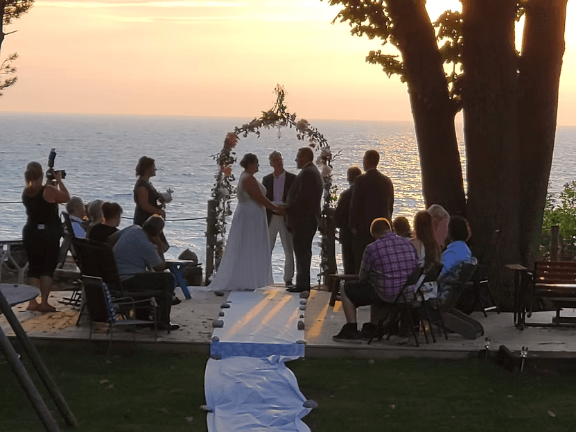 A couple exchanges vows at their wedding ceremony on a deck overlooking the ocean during sunset.