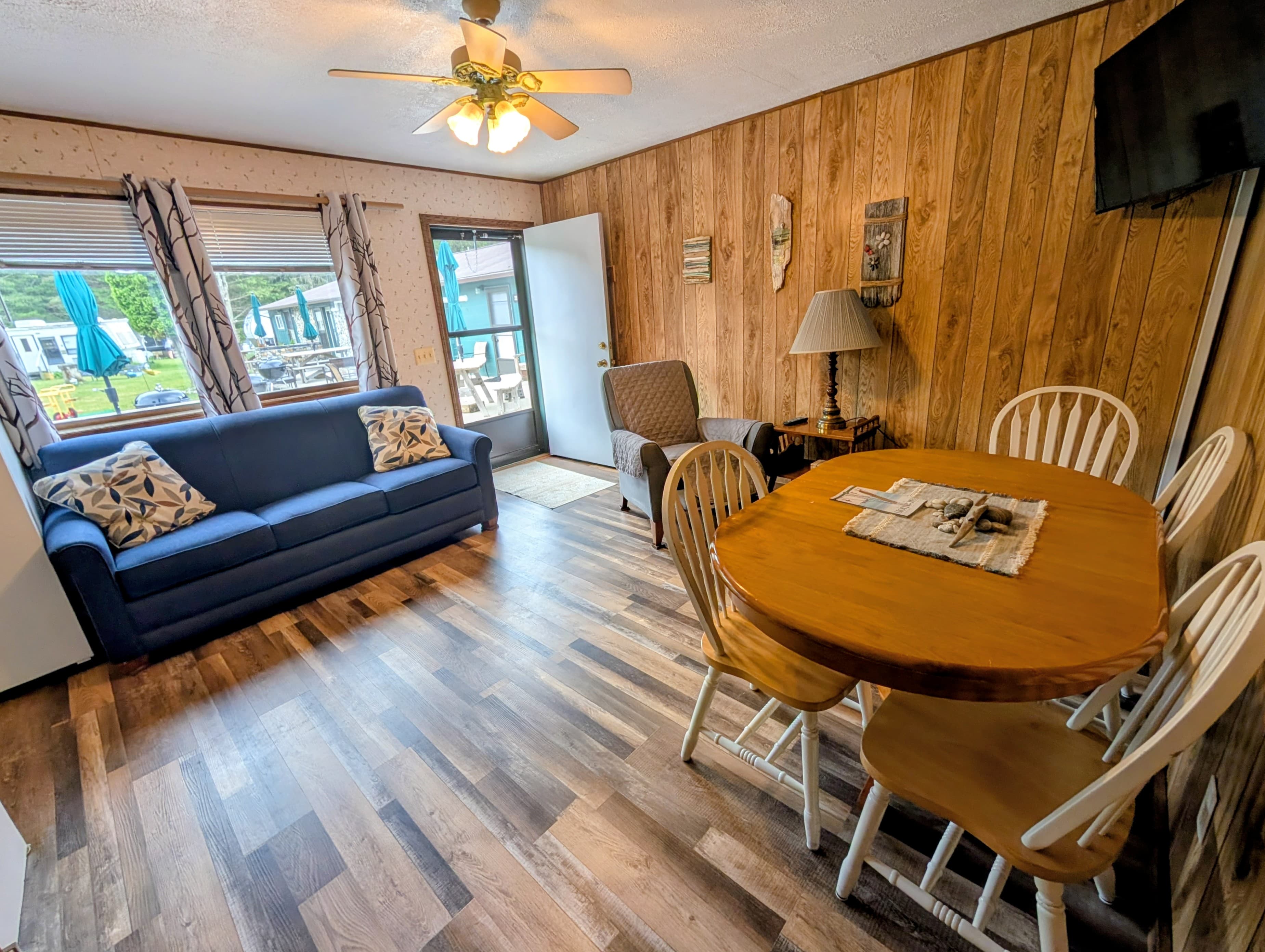 A cozy living area with a blue sofa, a dining table, and large windows letting in natural light.