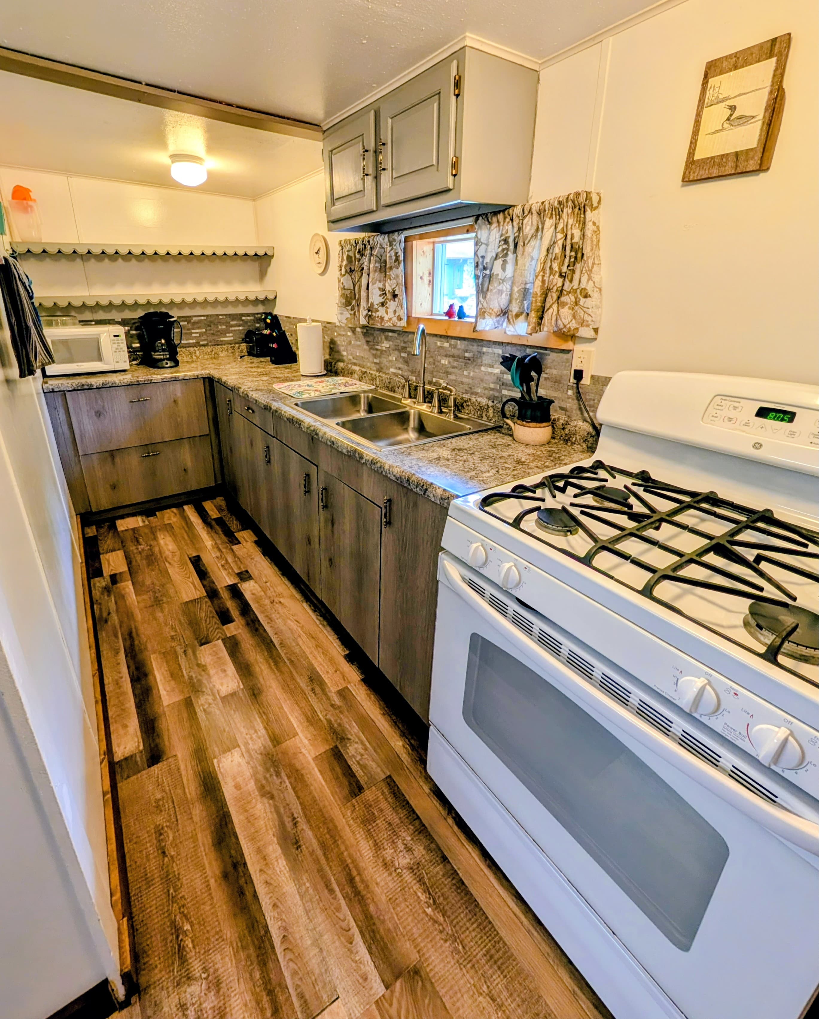 A modern kitchen featuring wooden cabinets, a double sink, a gas stove, and a decorative tile backsplash.