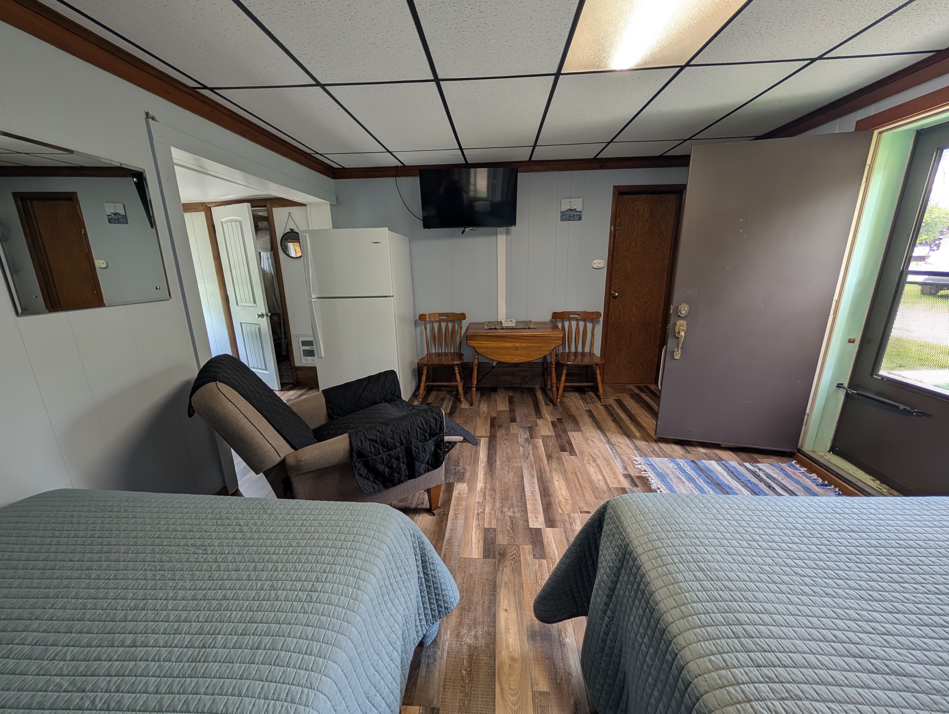 A cozy room with two beds, a chair, a table, a fridge, and a television.