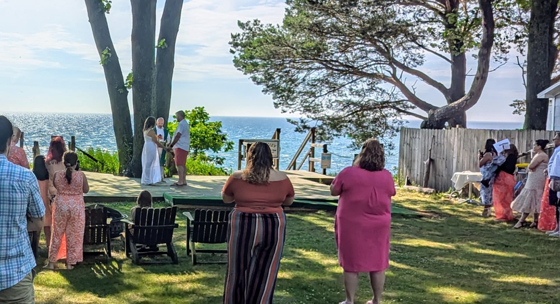A couple exchanges vows on an outdoor stage overlooking the ocean, surrounded by friends and family.