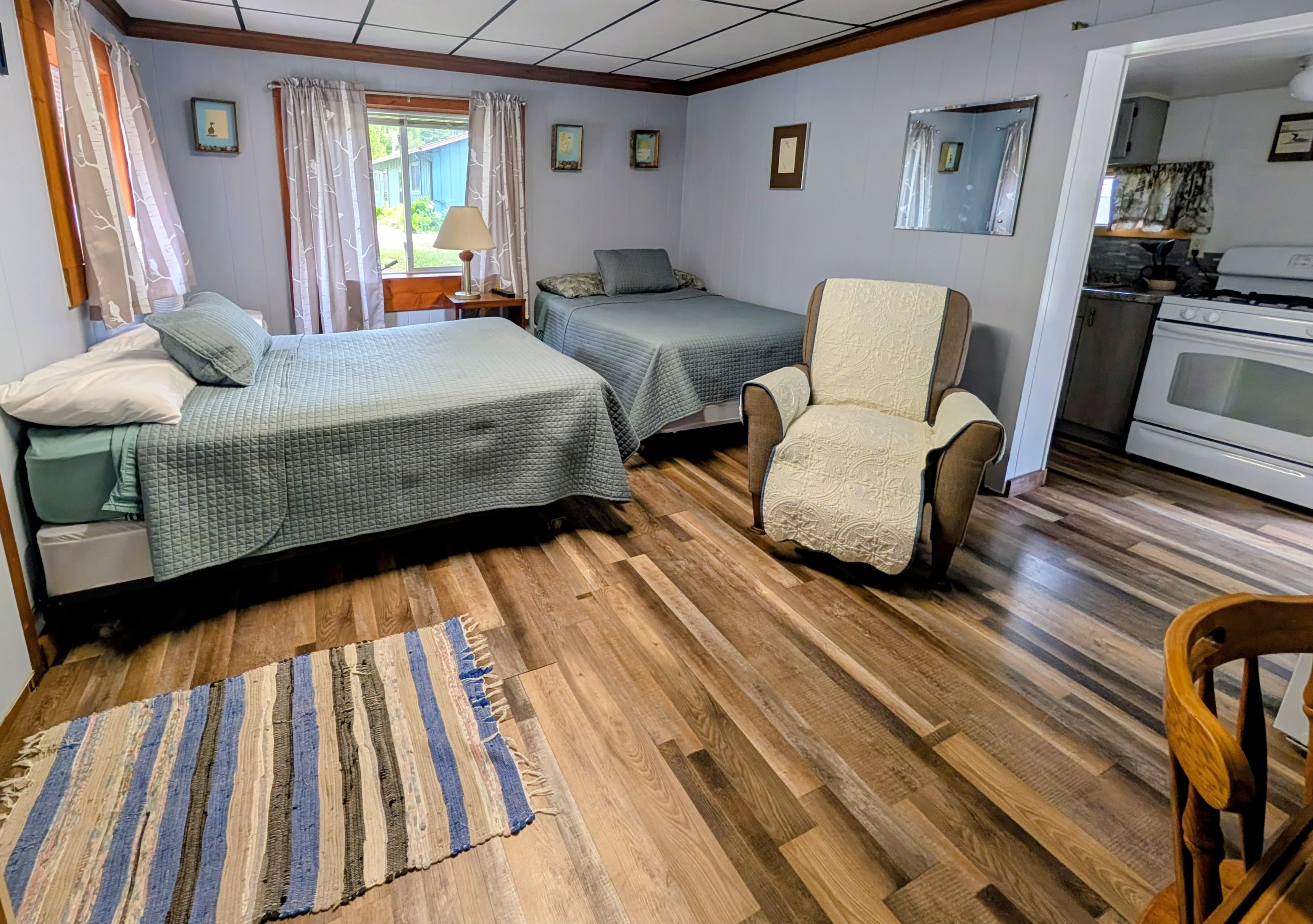 A cozy bedroom featuring two beds, a chair, and a small kitchenette in a rustic setting.
