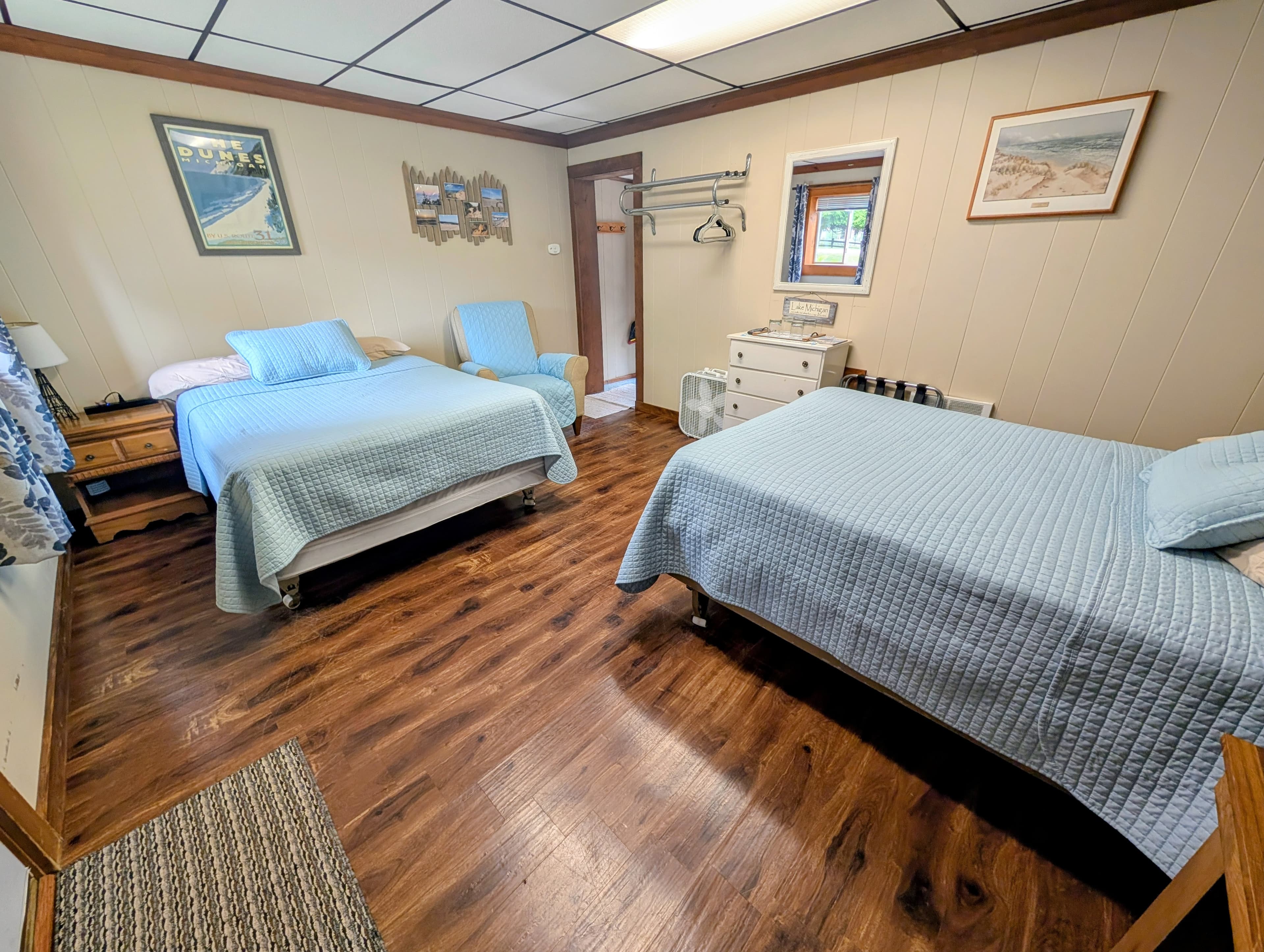 A cozy room featuring two blue-covered beds, wooden flooring, and warm decor.