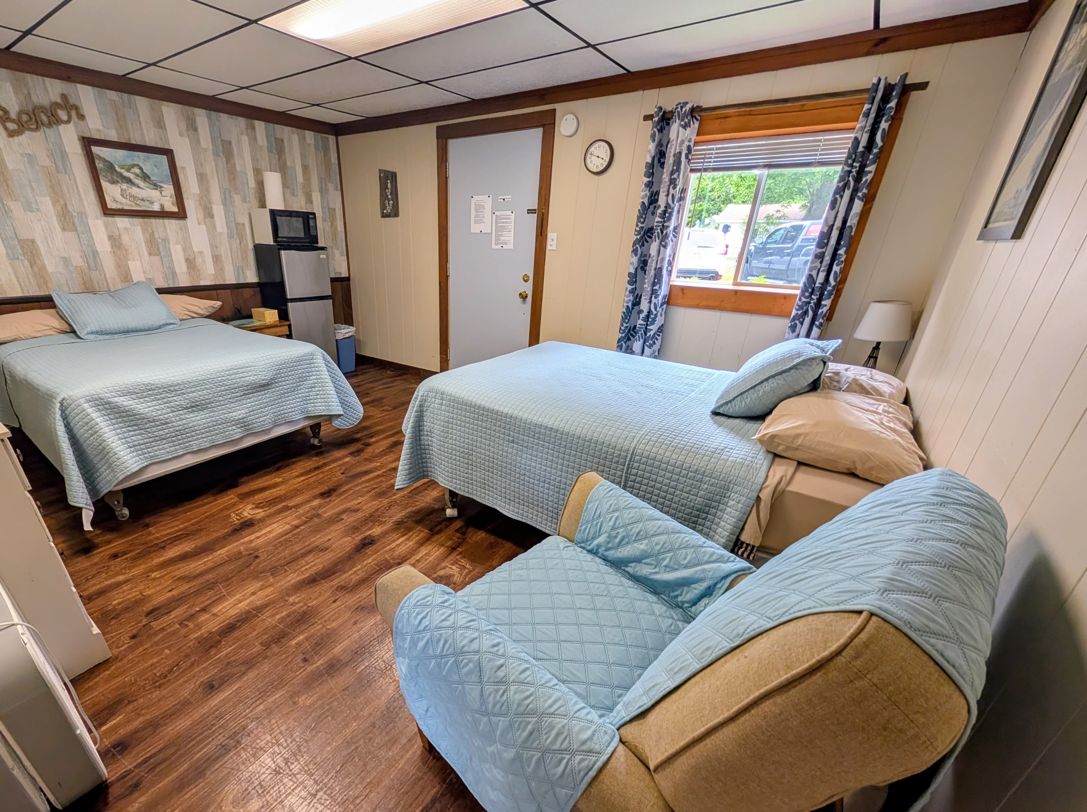 A cozy bedroom with two beds, a chair, and a small kitchenette.