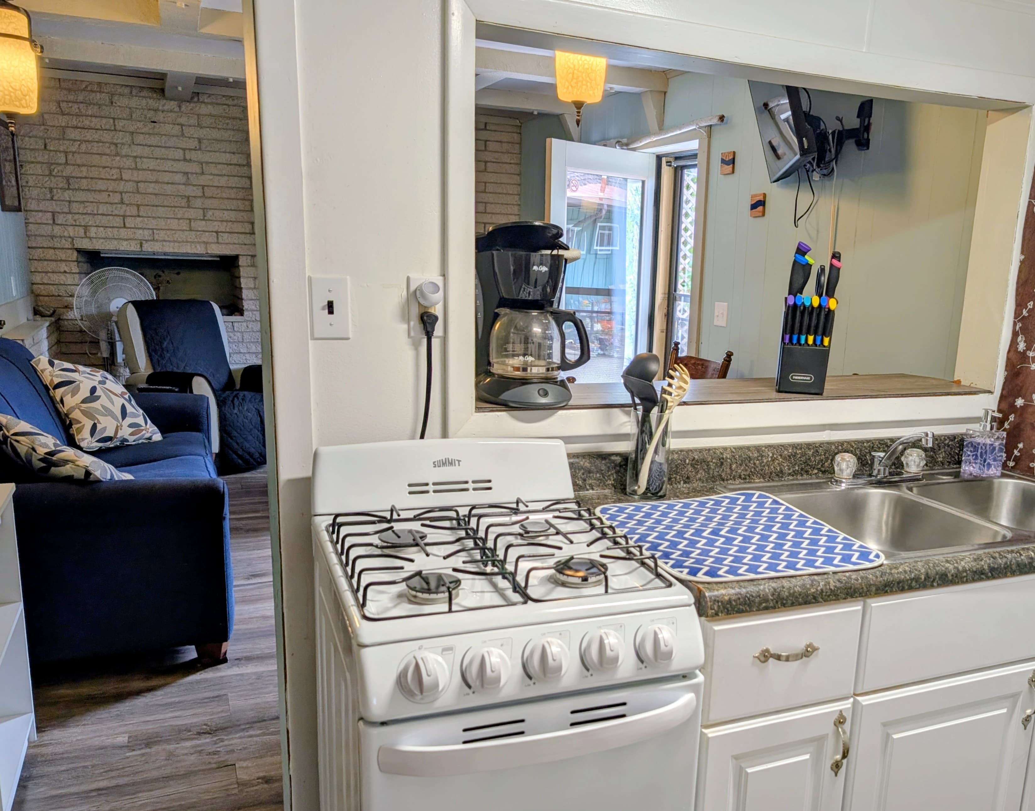 A view from the kitchen showcasing a gas stove, coffee maker, and a cozy living area beyond.