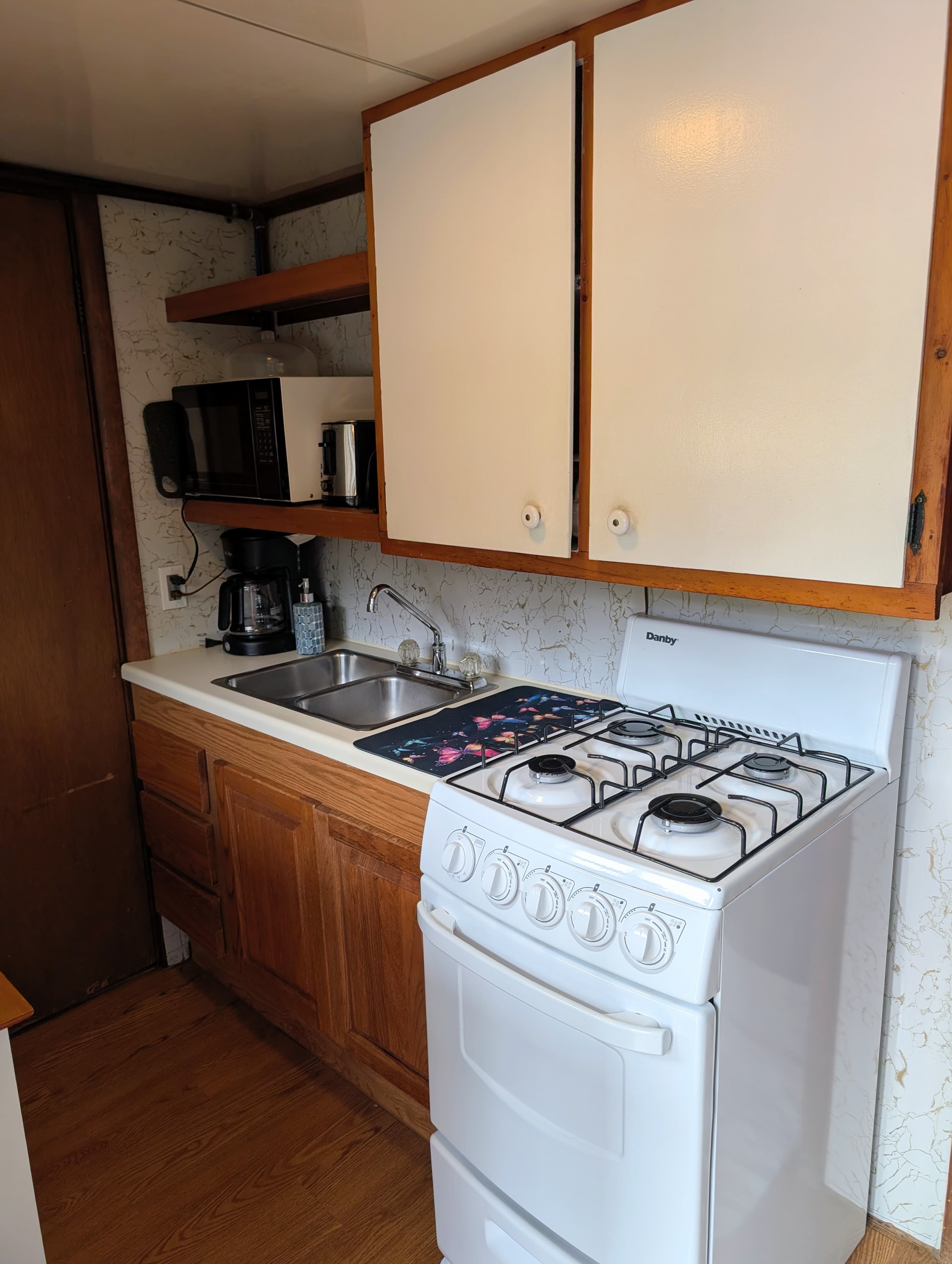 A compact kitchen featuring a gas stove, sink, microwave, and coffee maker with wooden cabinets.