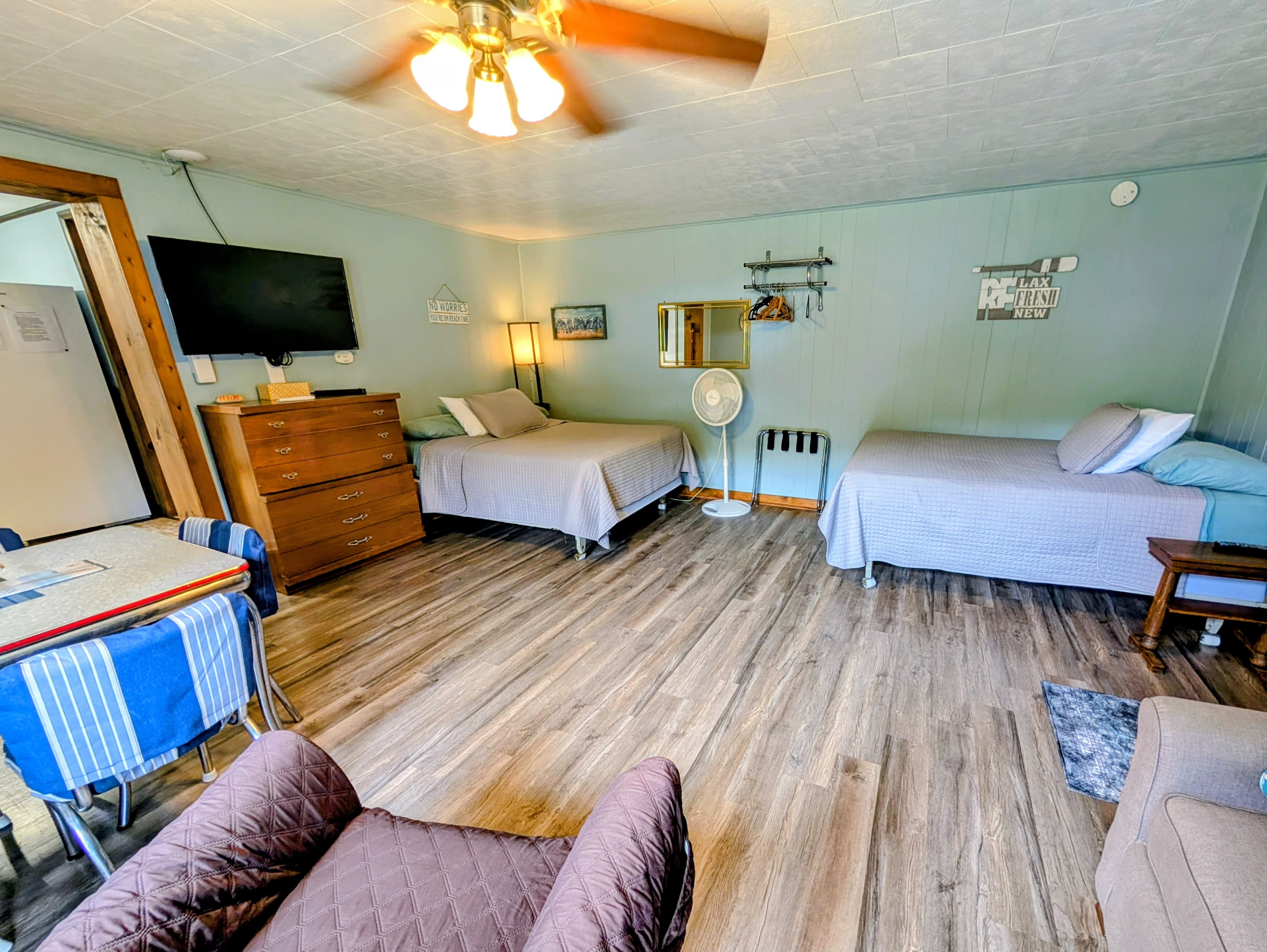 Cozy room featuring two beds, a television, and a dining area with a fan overhead.