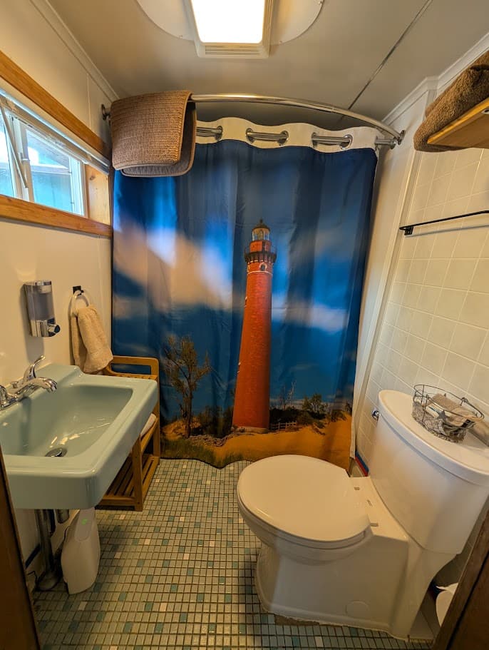 A small bathroom featuring a lighthouse-themed shower curtain, a light blue sink, a toilet, and tiled flooring.
