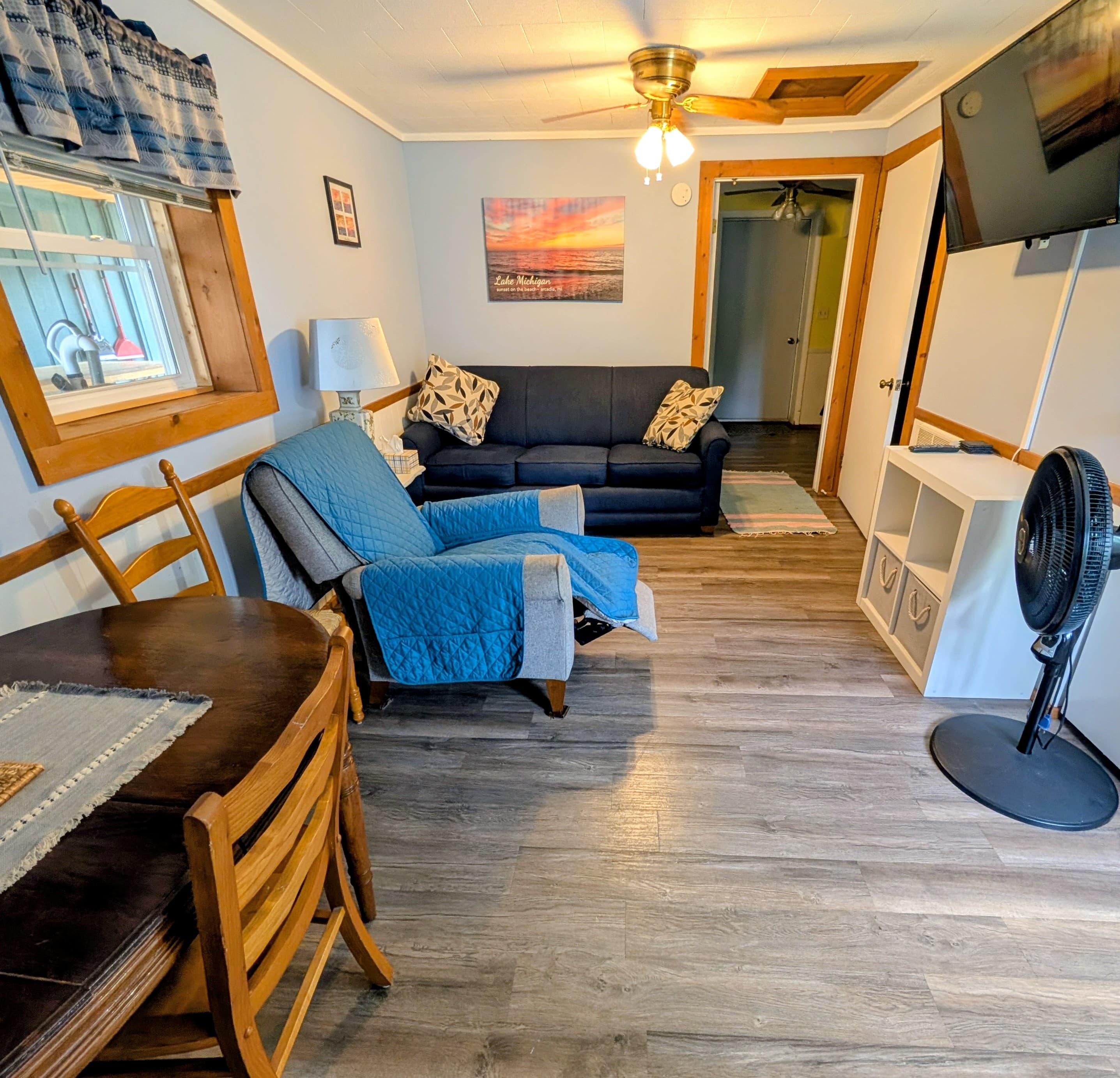 A cozy living room with a blue couch, a recliner, a dining table, and a TV.