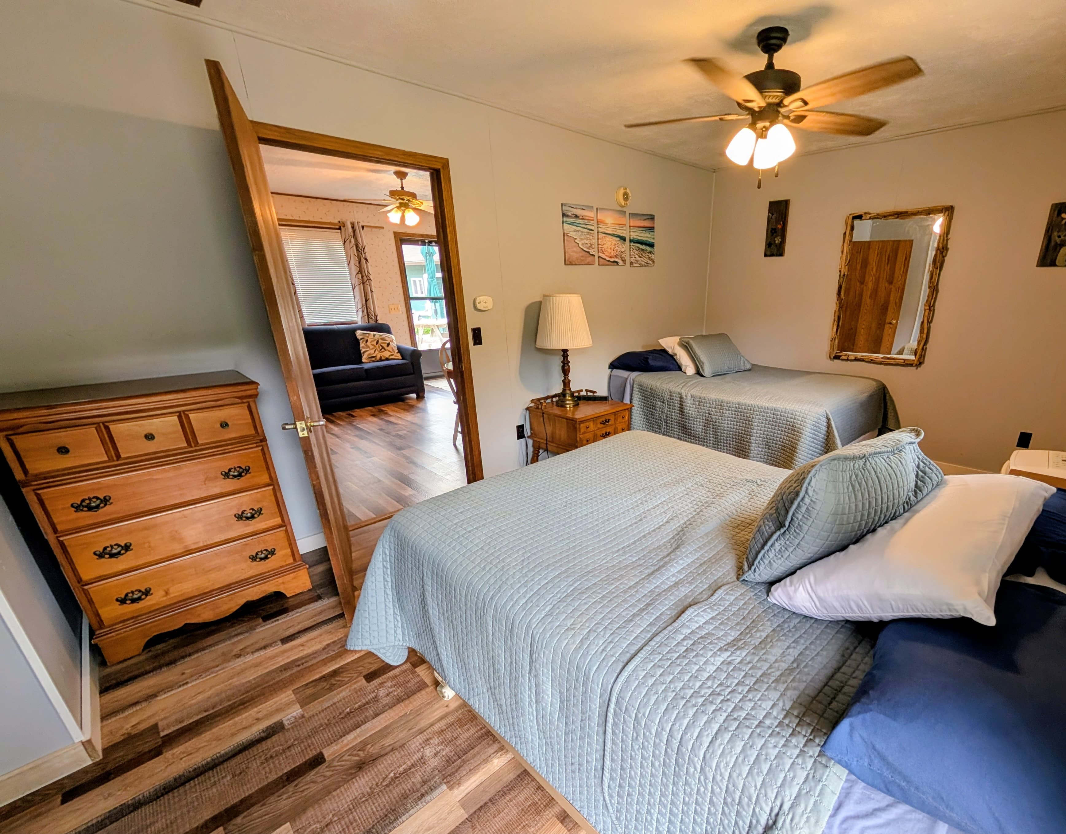 A cozy bedroom with two beds, a dresser, and a view into a living area beyond.